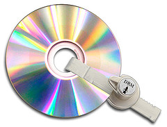 Um CD-ROM preso por um aloquete. O aloquete tem nele escrito a palavra DRM.